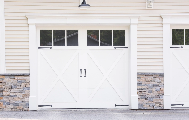 White carriage house garage door with crossbuck panels, upper windows, and decorative hardware
